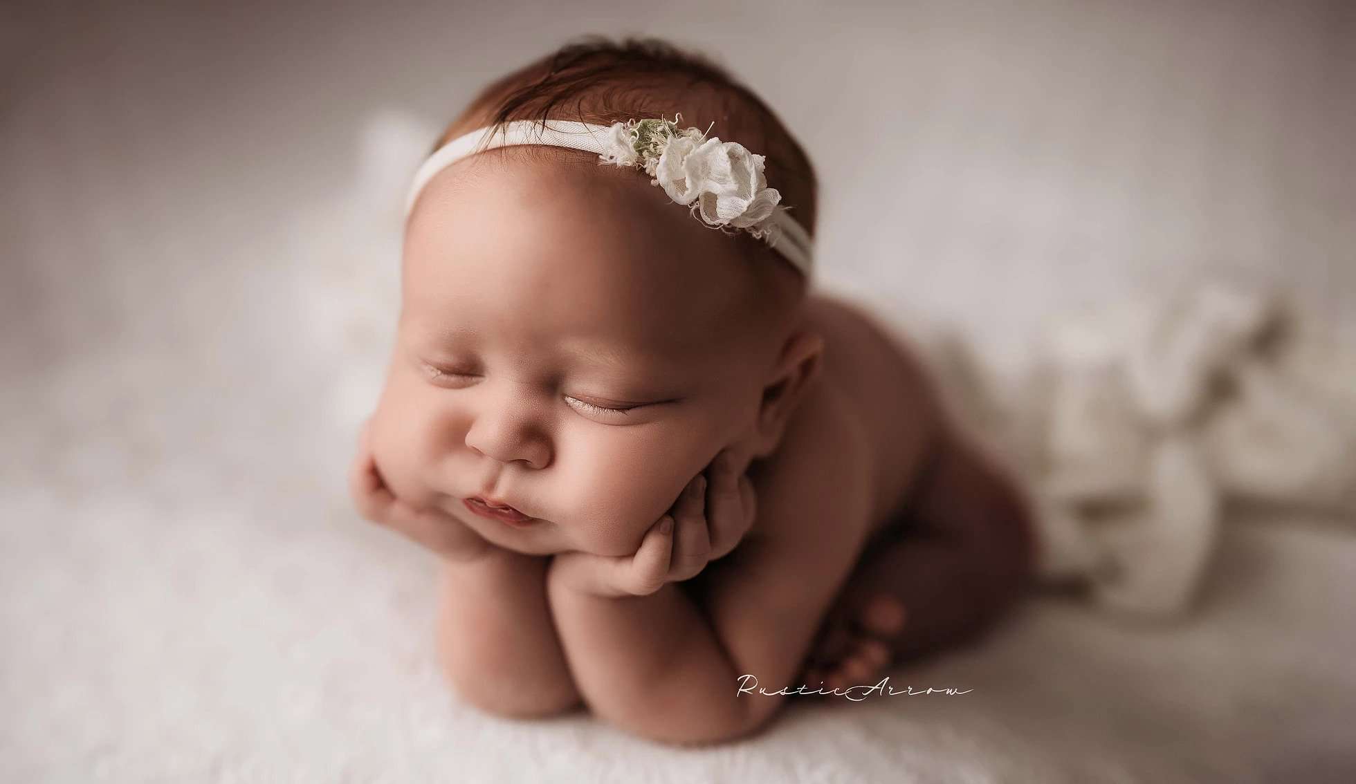 A newborn in Frog Pose on a white blanket in a studio