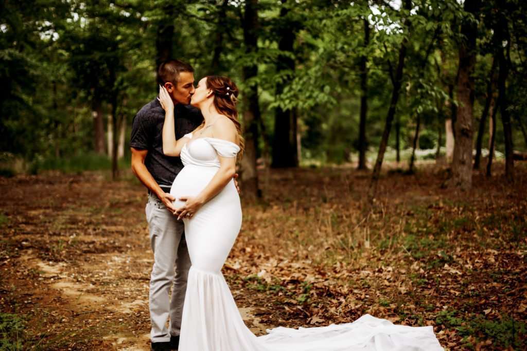 pregnant woman kissing her husband while cradling her baby during her Crystal Bridges maternity photography session