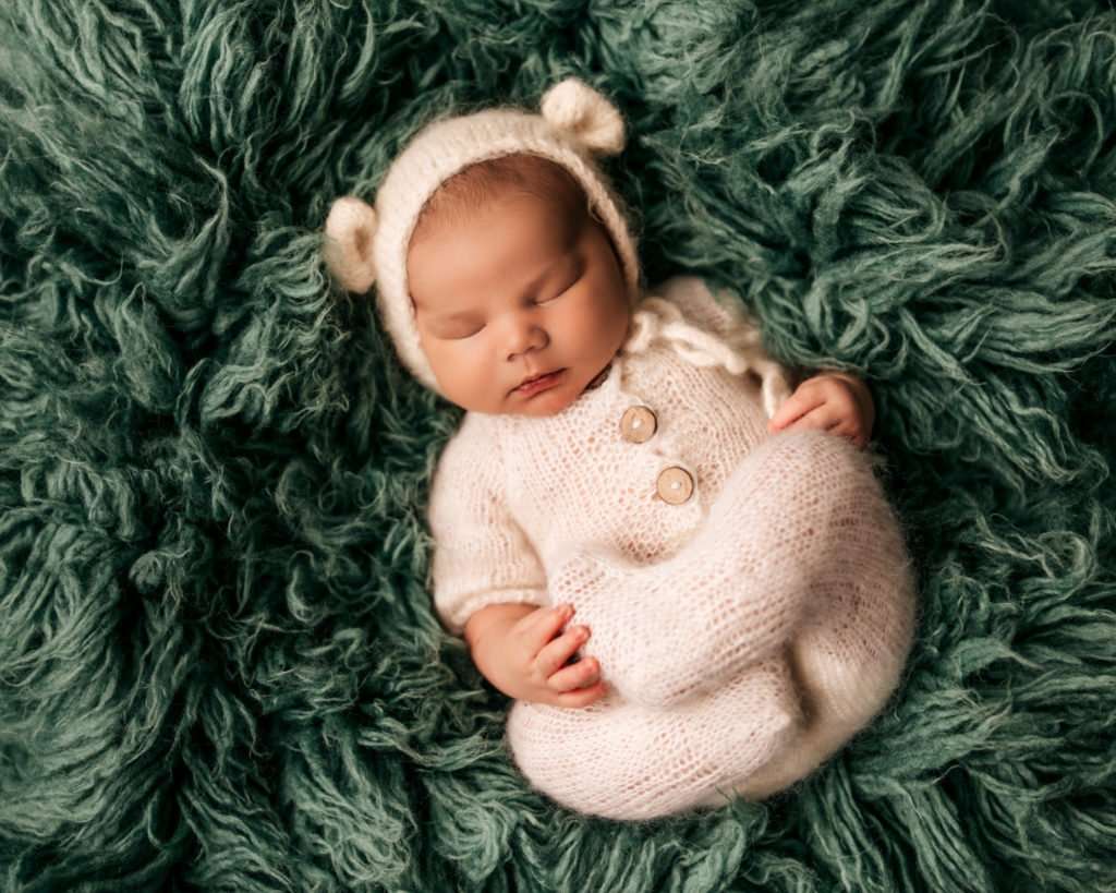 Baby in knit outfit with bear ear bonnet on a green flokati for newborn photography images