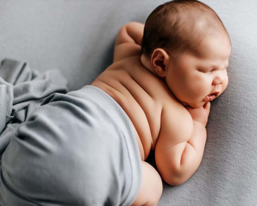 baby on blue backdrop laying on belly with back rolls showing for newborn photography images