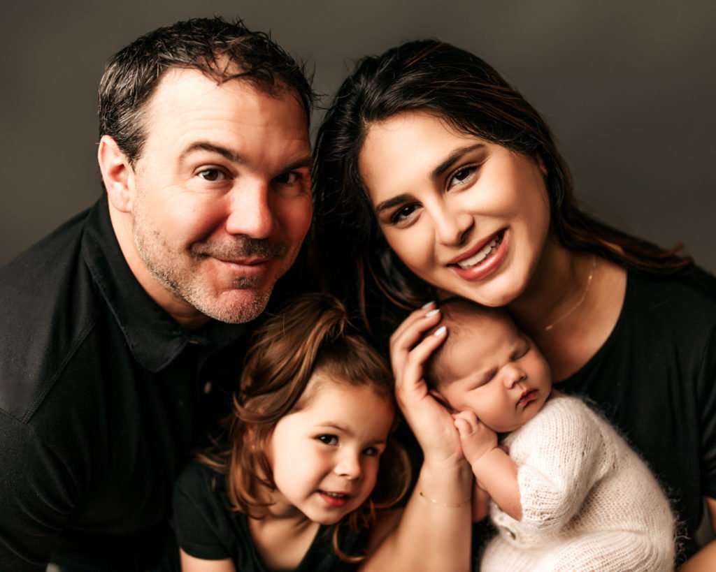 family posed with dark gray backdrop for newborn photography