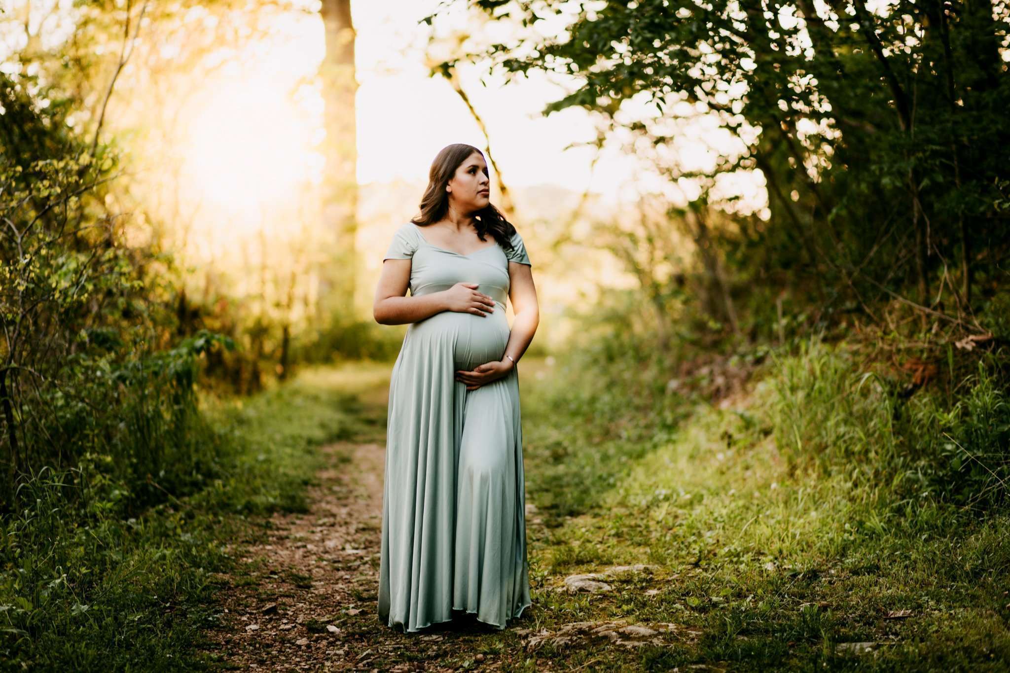 Pregnant mom standing in wooded area holding baby belly in green dress