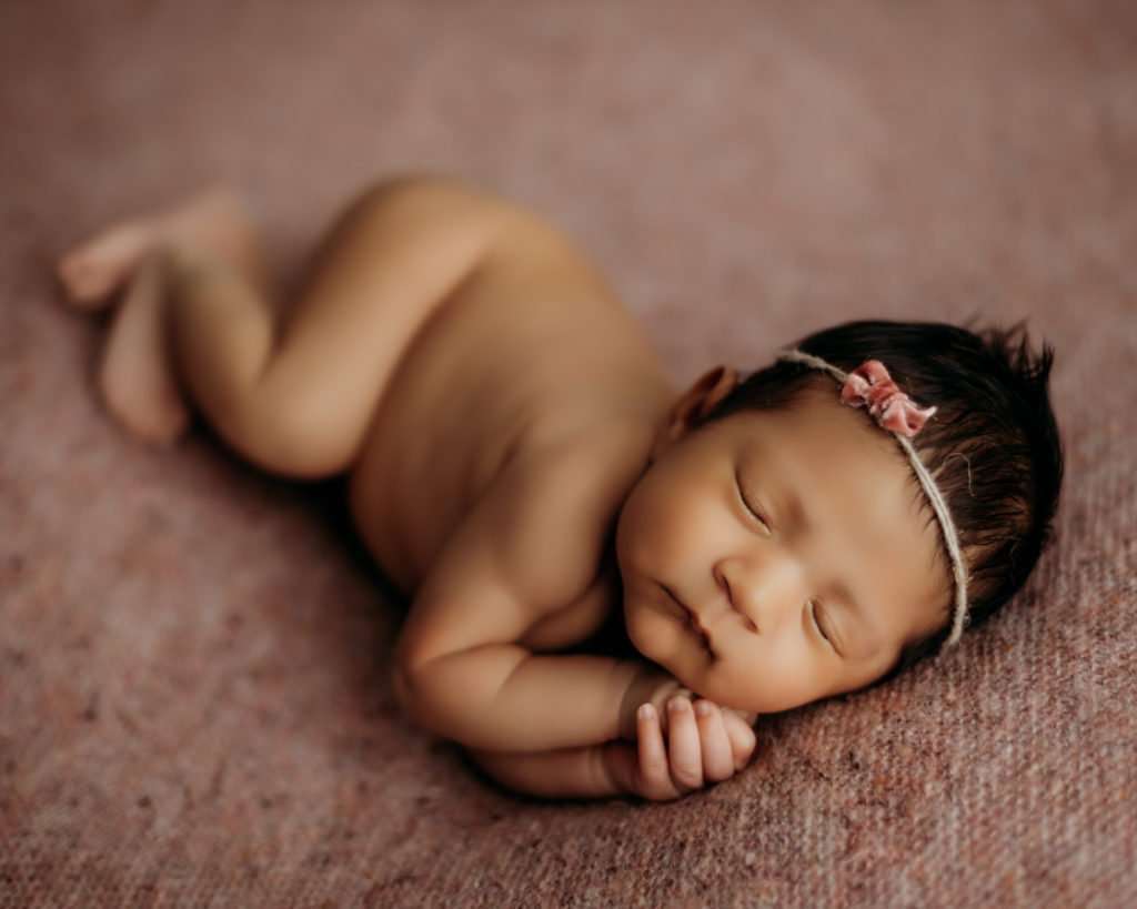 newborn on pink textured backdrop in a sleeping pose during newborn photography session