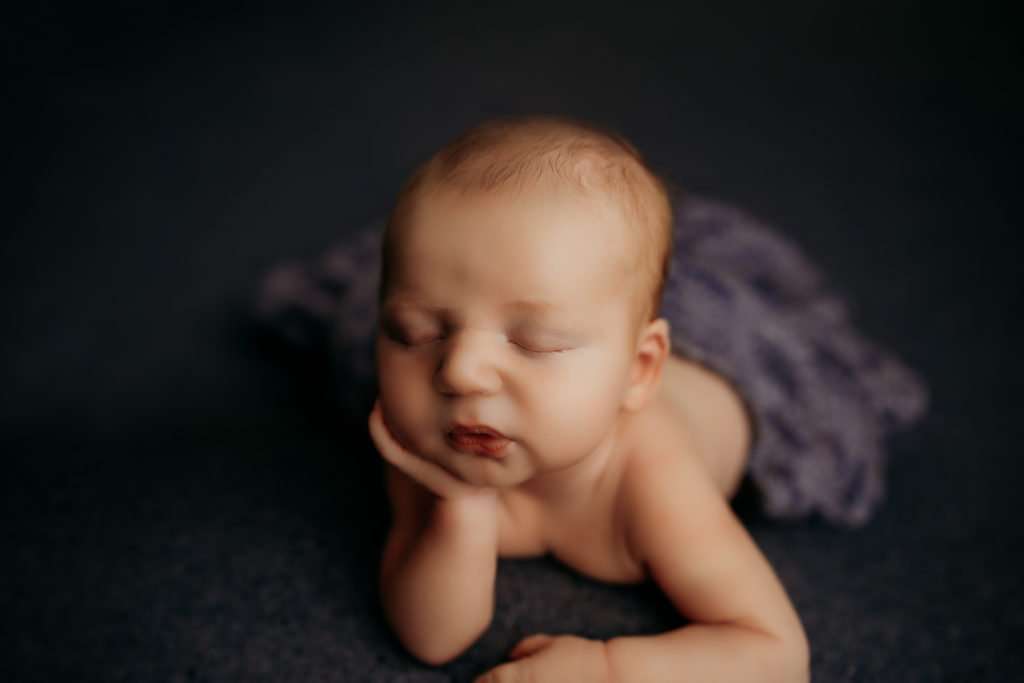 newborn on dark blue backdrop resting his chin on his hand looking like he's bored