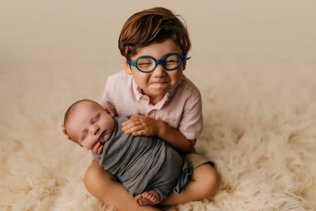 big brother holding wrapped up little brother giving a silly smile