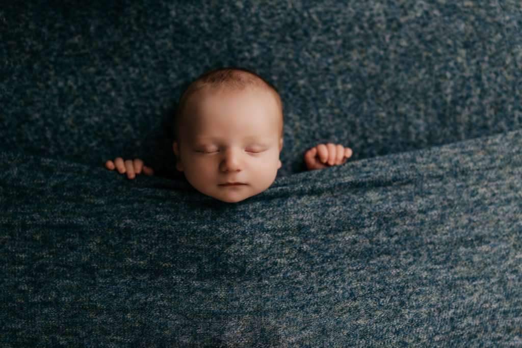 baby in tucked in pose during newborn photography session on dark blue textured backdrop sleeping